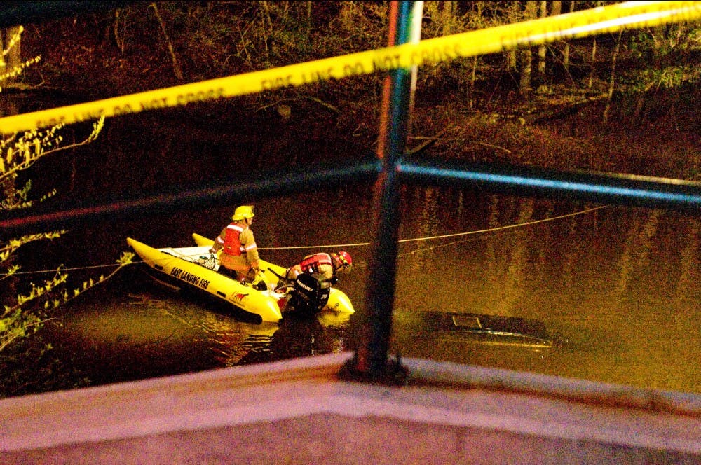 Rescue workers survey the submerged dark Buick early Friday morning on the Red Cedar River near the intersection of Grand River Ave. and Hagadorn Road.  Jaclyn McNeal/The State News