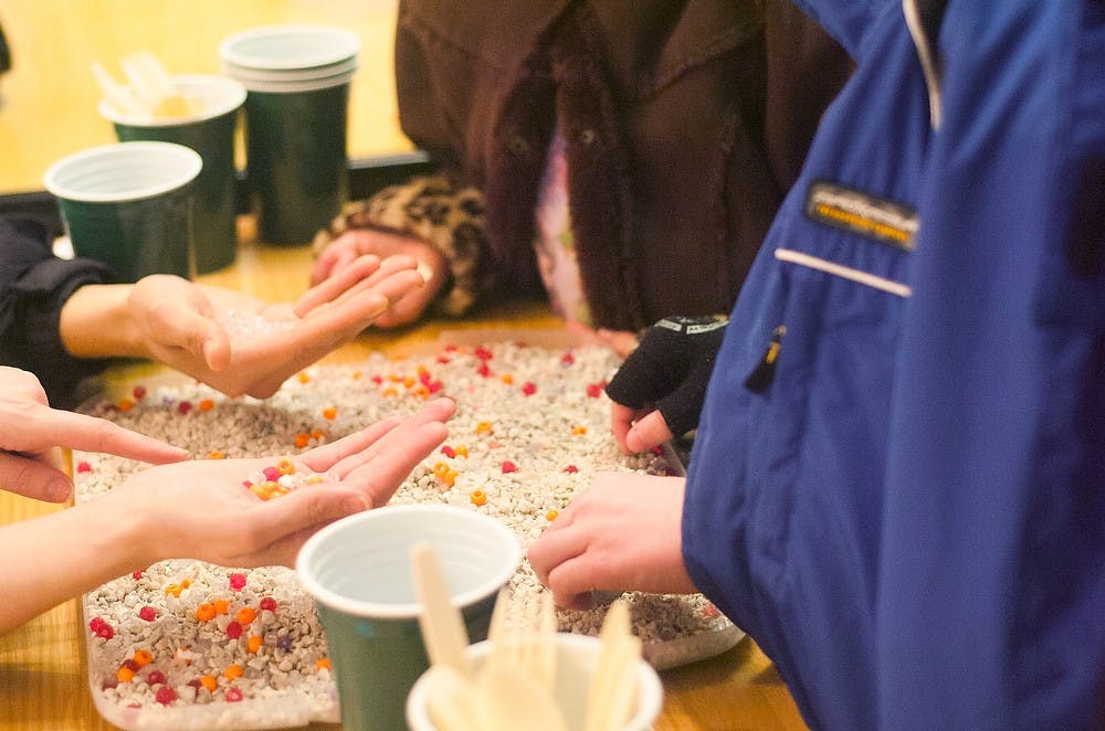 	<p>Volunteer Liliana Lettieri teaches Ava, 8, and Baisil Mullen, 9, about the process of natural selection by playing a game where the children scooped beads of multiple colors out of a tray of gravel Feb. 9, 2014, at the <span class="caps">MSU</span> Museum. The game was a part of Darwin Discovery Day. Sierra Lay/The State News</p>