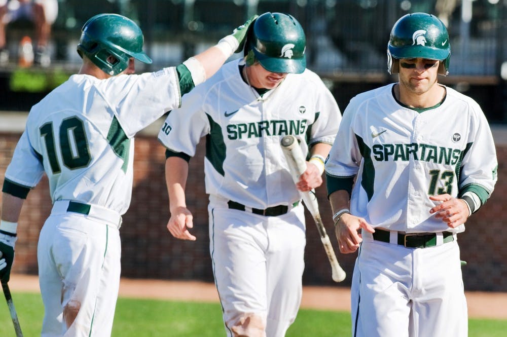 Junior infielder Ryan Jones, left, pats the helmet of junior outfielder and infielder Jared Hook after Hook and senior shortstop Justin Scanlon, right, score one run each. The Spartans defeated the Broncos, 13-3, Tuesday afternoon at McLane Baseball Stadium at Old College Field. Justin Wan/The State News