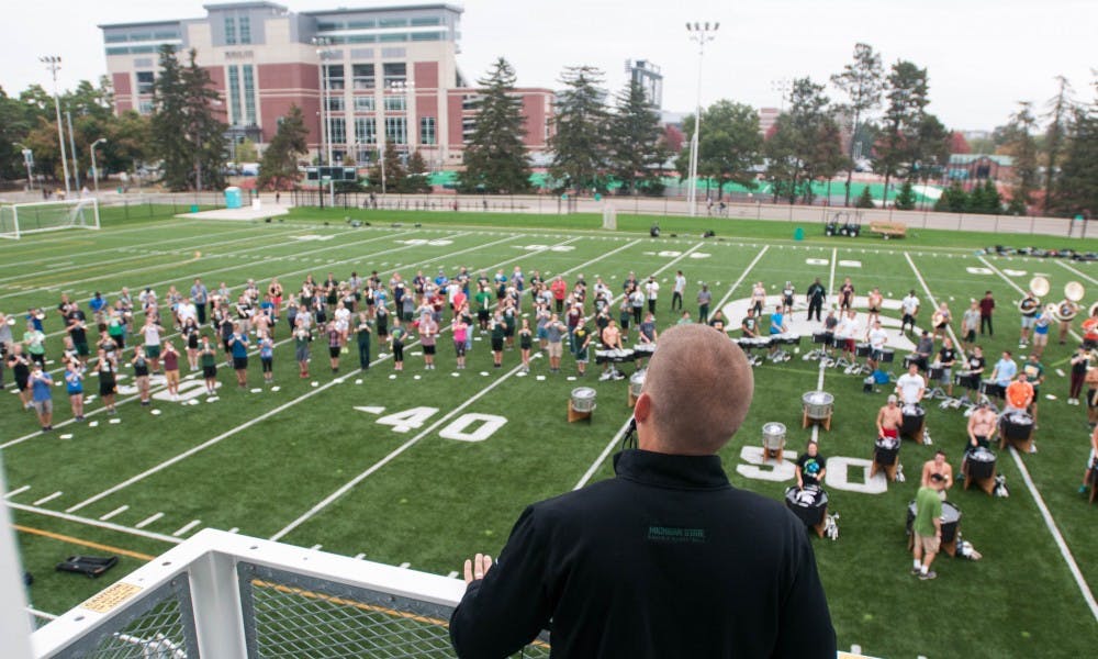 MSU marching band director David Thornton stands above the band during Spartan Marching Band practice on Sep. 19, 2017 at Munn Field. Throughout the practice, Thornton jumped to the tempo, shouted praise at the students and sang along to the music.