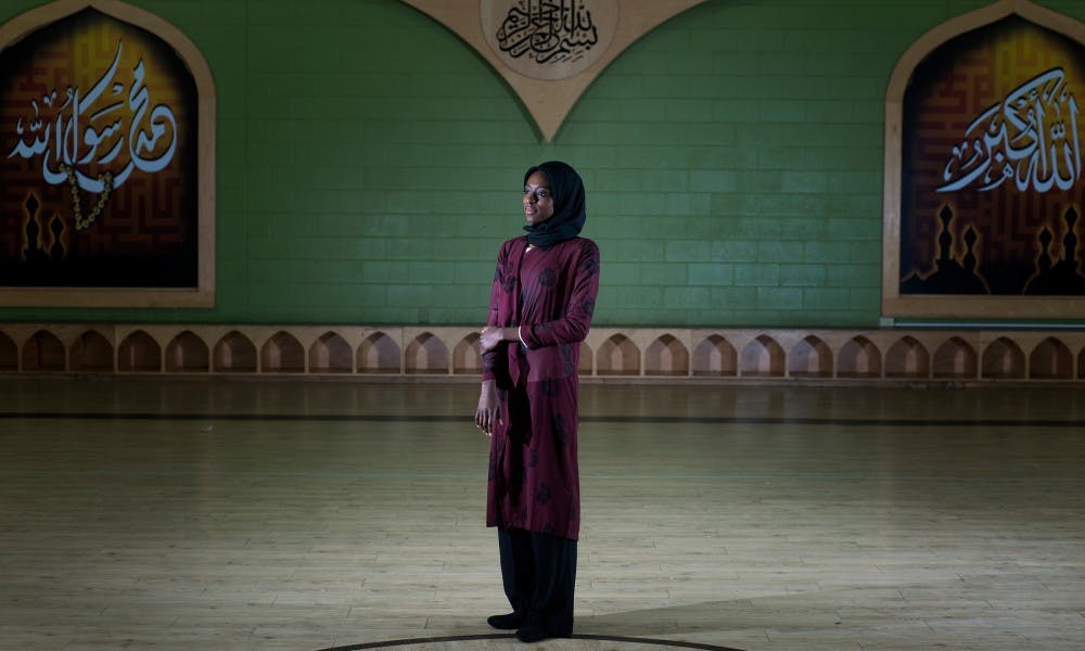 Advertising junior Hauwa Abbas poses for a portrait on Nov. 27, 2015 inside the gymnasium of the Islamic Society of Greater Lansing. Abbas works to help bring cultural understanding among Muslims and non-Muslims. The text to her left means "Muhammad is the messenger of God." The text above, "In the name of God, the most beneficent, the most merciful." The text to her right, "God is the greatest."