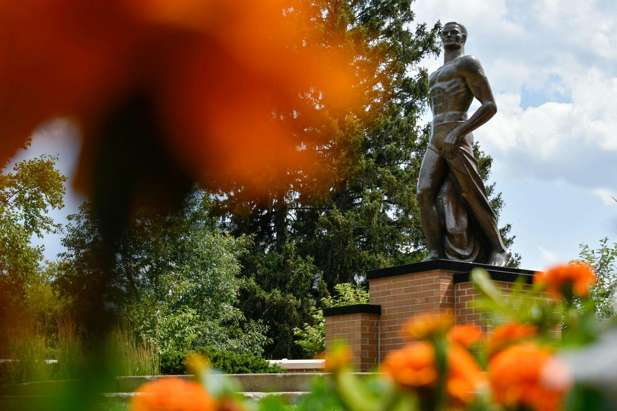Orange and white flowers surround the Spartan Statue on July 19, 2023.