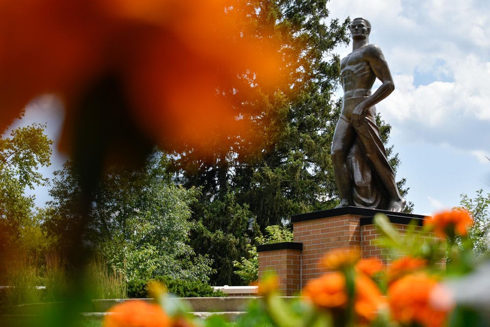 Orange and white flowers surround the Spartan Statue on July 19, 2023.