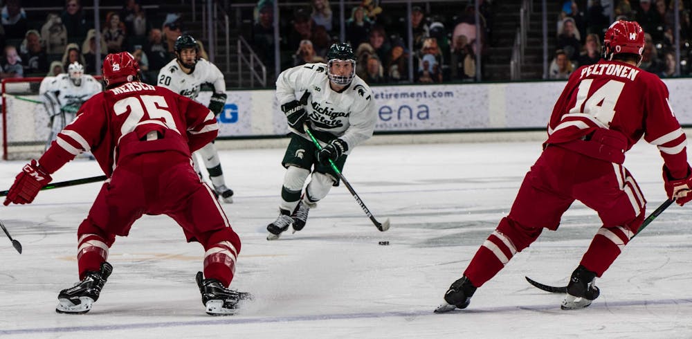 <p>Graduate student forward Charlie Combs (7) takes the puck back from the Michigan State goaltender and skates down the ice in the first period. The Badgers shut out the Spartans 4-0 at Munn Ice Arena on March 5, 2021. </p>