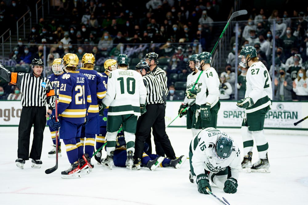 <p>Michigan State senior Christian Krygier and Notre Dame junior Solag Bakich are hurt on the ground with both teams being present as they start to get up on Feb. 19, 2022. Spartans lost 4-2 against Notre Dame.</p>