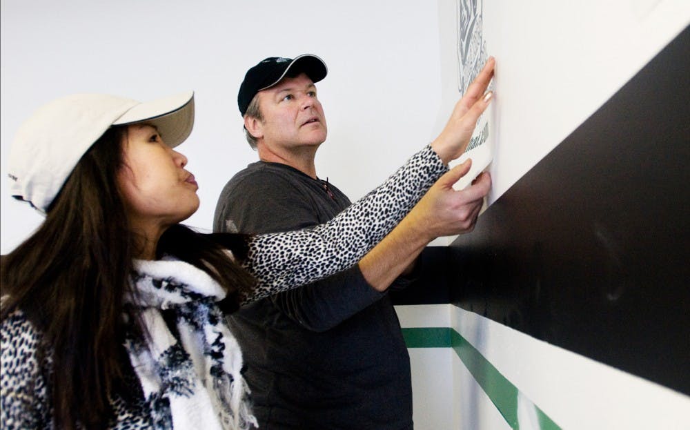 Owners of Spar-thai David and Tripiadub Thorin smooth out a wall decal Thursday afternoon at their Albert St. store front. Spar-thai is a laundry and bike taxi hybrid offering students timely cleaning and a cheaper alternative to standard cabs. Matt Hallowell/The State News