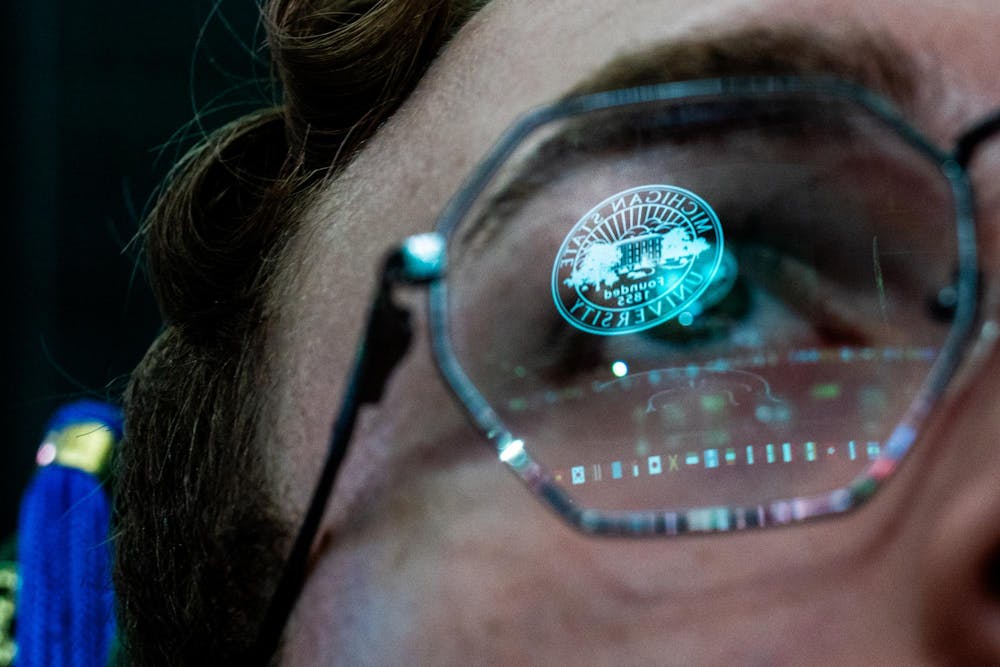 The Michigan State emblem is reflected in a graduate’s glasses during the Michigan State University College of Communication Arts and Sciences graduation ceremony at the Breslin Student Events Center on Michigan State University’s campus in East Lansing, Mich., on Friday, May 1, 2026.