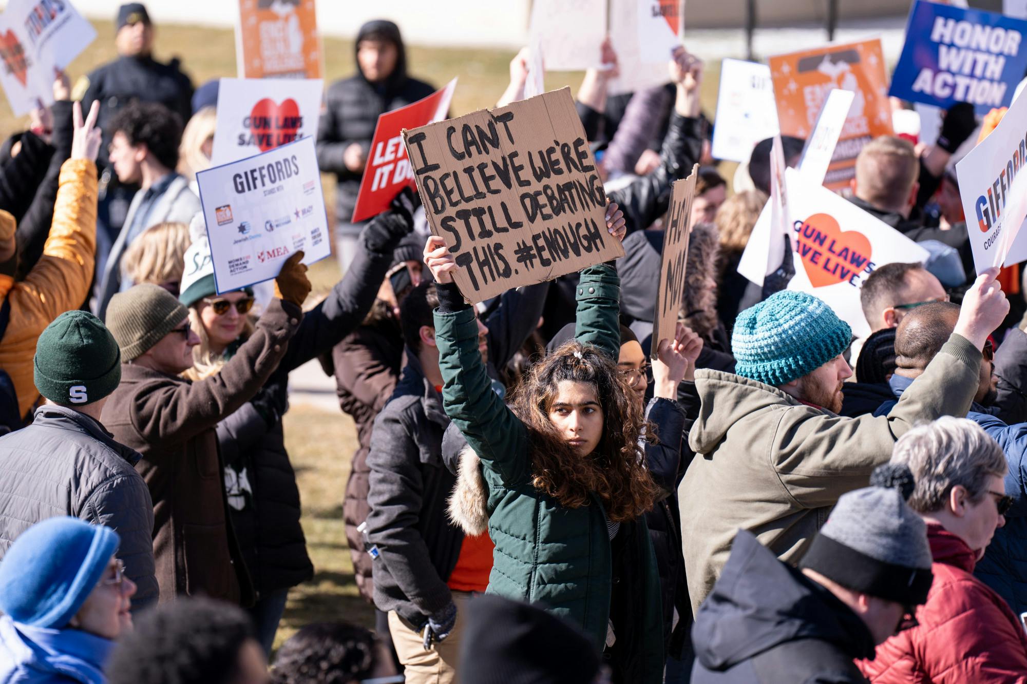 <p>A protestor holds a sign saying "I can't believe we're still debating this. #ENOUGH" at the Gabby Giffords gun rally at the Michigan State Capitol on March 15, 2023.</p>