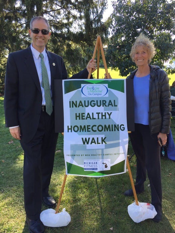 <p>Dean of Arts and Letters, Christopher Long, left, stands by the Inaugural Healthy Homecoming Walk sign. This walk&nbsp;was a health initiative hosted by Exercise is Medicine on Campus. Photo courtesy of Kerri Vasold&nbsp;</p>