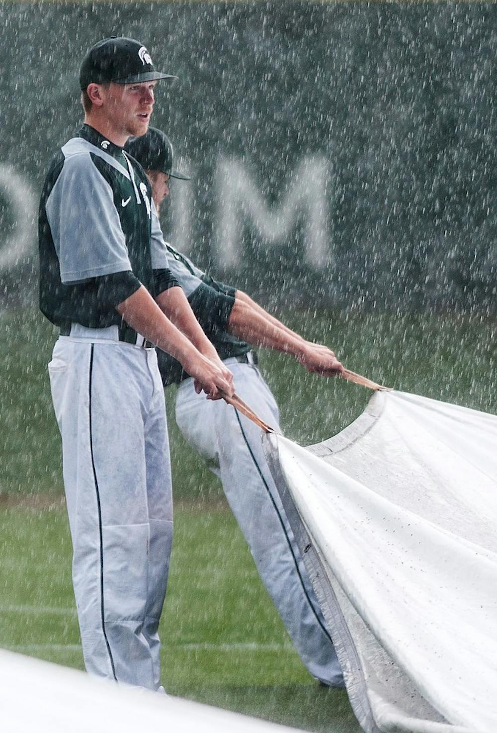 <p>Freshman pitcher Walter Borkovich helps his teammates cover the field with tarp before the game against Nebraska on May 12, 2014, at McLane Baseball Stadium at Old College Field. The game was called due to lightning in the bottom of the eighth, and the Cornhuskers defeated the Spartans, 4-1. Corey Damocles/The State News</p>