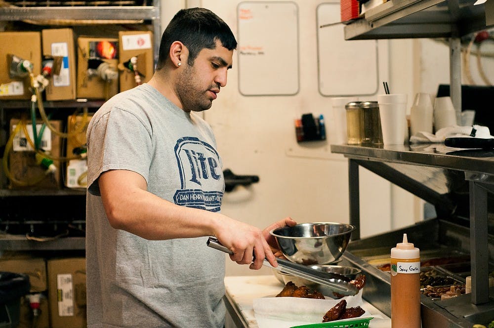 <p>East Lansing resident Adam Rosales plates wings Jan. 29, 2015, during his shift at Crunchy's, 254 W. Grand River Ave. in East Lansing. Crunchy's has been around for 33 years. Hannah Levy/The State News</p>