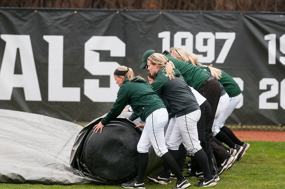 	<p>The <span class="caps">MSU</span> softball team rolls up the tarp that was used to protect the infield before the game against Michigan, April 14, 2013, at Secchia Stadium at Old College Field. The game was delayed by snow and rain for an hour. Katie Stiefel/The State News</p>