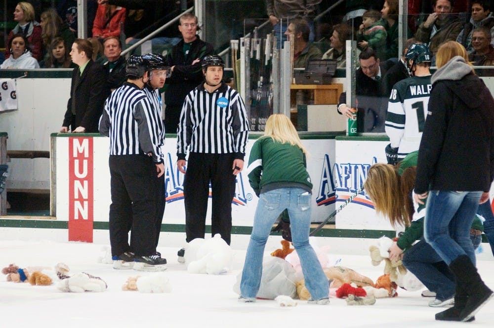 Workers pick up teddy bears on ice thrown by the audience as donations to local charities after the MSU scored the first goal. The Michigan State Spartans defeated the Northern Michigan Wildcats, 2-1, Saturday night at Munn Ice Arena. Justin Wan/The State News