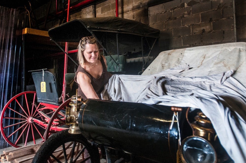 Lynne Swanson, collections manager for cultural collections, removes the cover to Ransom E. Olds' personal 1903 Oldsmobile Friday, Aug. 3, 2012 in the Spartan Stadium storage facility. The car has been held in storage since 1990. Adam Toolin/The State News