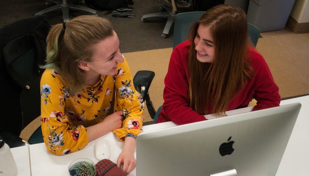 Campus reporter Claire Moore, left, and cops and courts reporter Anna Nichols, right, laugh at a desk at the State News office on Feb. 13, 2019.