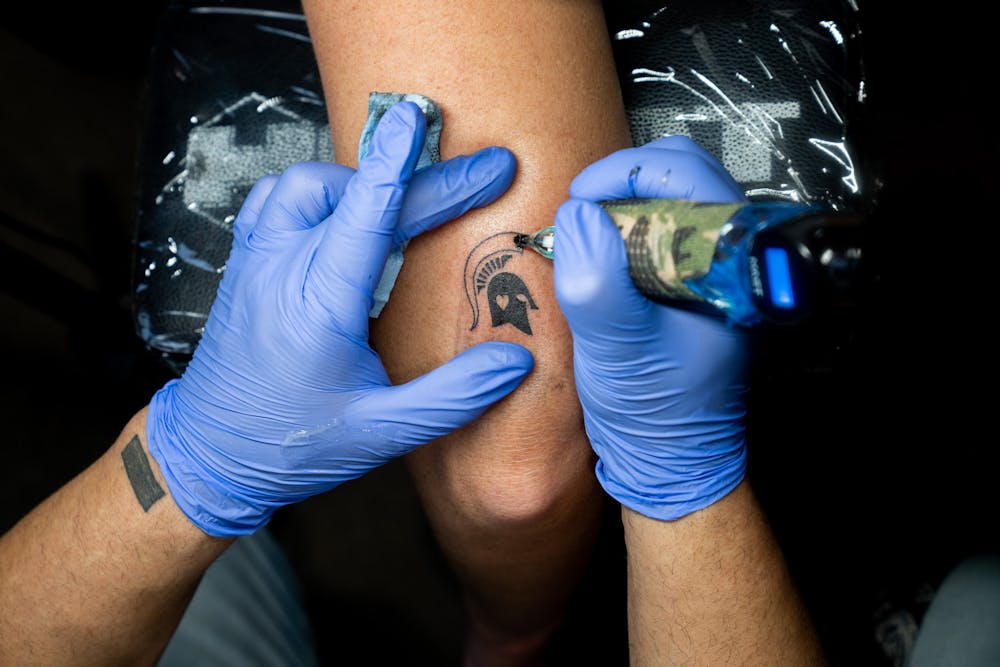 Tattoo Artist Alex Martinez tattoos the Spartan helmet onto customer and mental healthcare worker, Chelsea Ghastin during the Spartan Strong event at Ink Therapy on Feb. 19, 2023. 
