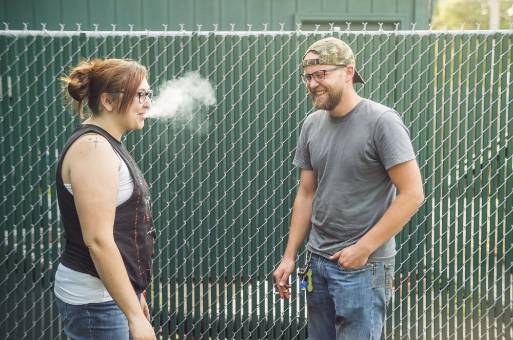 Lansing resident Emma Hoierville and Lansing resident Sam Holoweiko smoke together on Aug. 15, 2017, outside of Crunchy's bar in East Lansing.