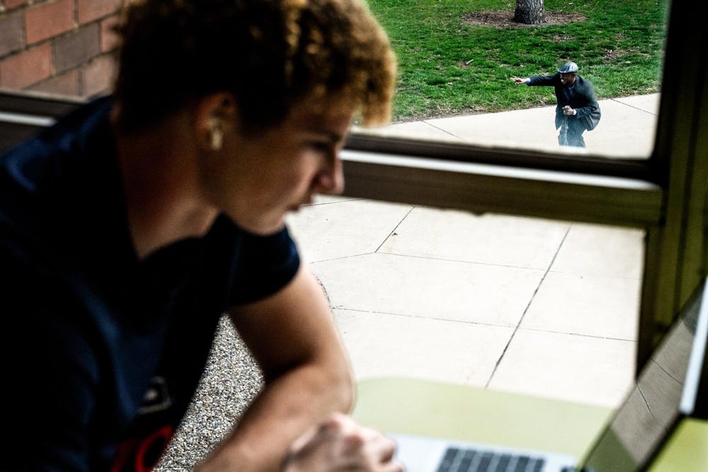 Michigan State University business freshman Logan Aguirre, 18, works inside Wells Hall while Pastor Michael Venyah preaches outside in People’s Park, seen through a window on Michigan State University’s campus in East Lansing, Mich., on Monday, April 13, 2026.