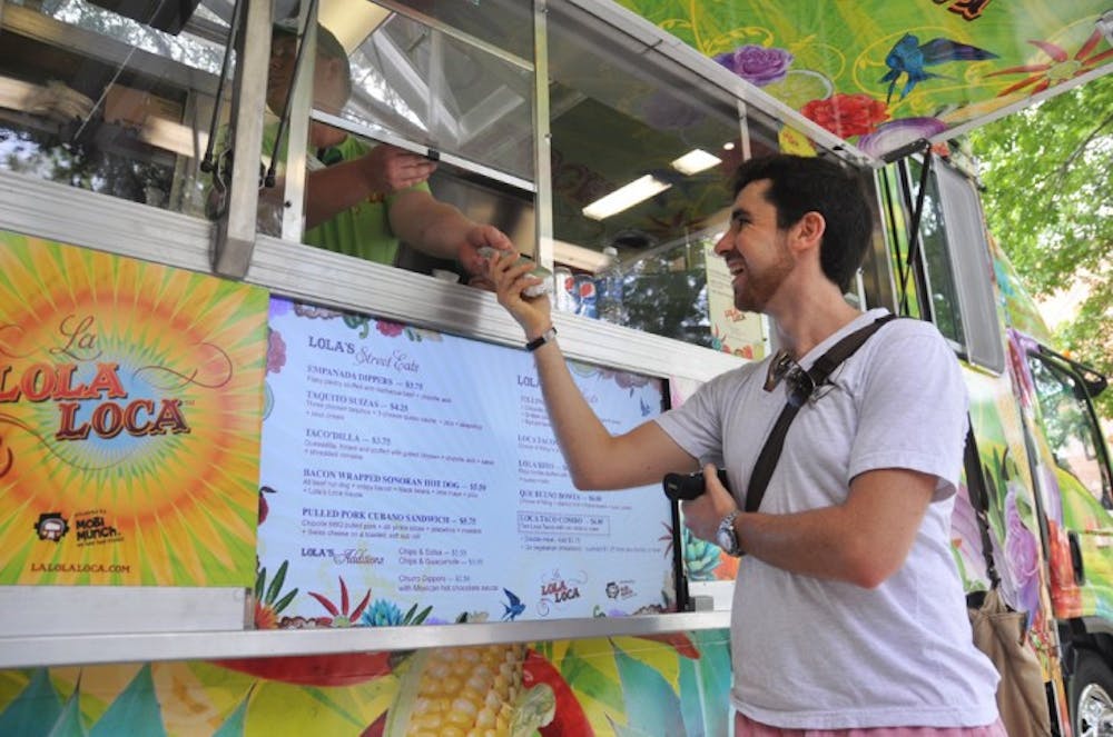 <p>Stefan Wolff, a 20-year-old economics junior, grabs a pulled pork cubano candwich for lunch at the La Lola Loca food truck near the Plaza of the Americas on Tuesday.</p>