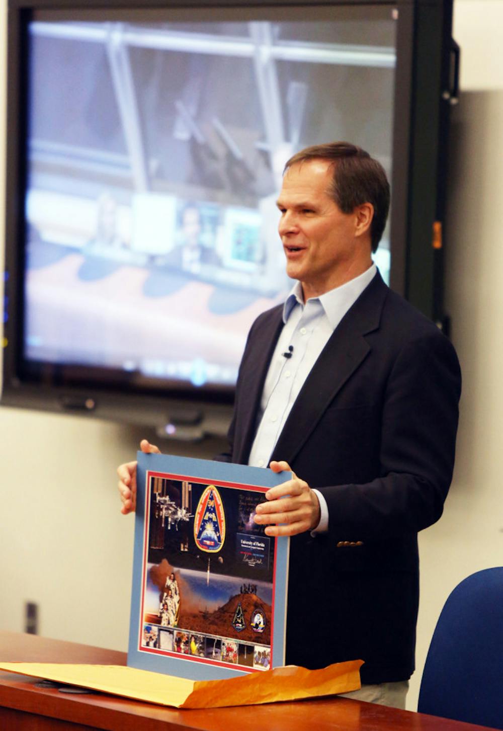 <p>Retired astronaut Kevin Ford presents an Expedition 34 mission patch that was flown in space.</p>