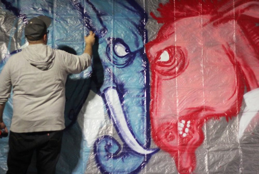 <p>Evan Poirier, 30, spray paints a political mural in support of First Friday: Red, White and Vote downtown on Friday night. “I wanted something bipartisan that would get people out and voting,” Poirier said.</p>