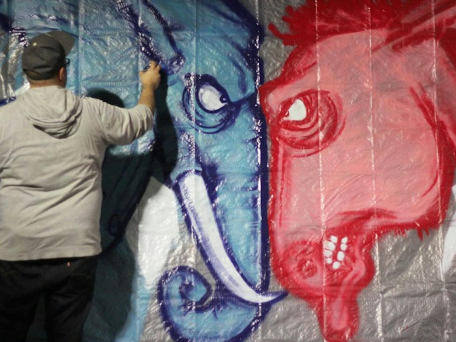 Evan Poirier, 30, spray paints a political mural in support of First Friday: Red, White and Vote downtown on Friday night. “I wanted something bipartisan that would get people out and voting,” Poirier said.