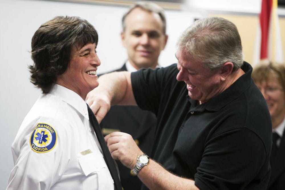 <p>Elizabeth J. Braun receives a badge from her husband, George Braun, in honor of her promotion to lieutenant at a ceremony promoting Gainesville Fire Rescue members at about noon Thursday at the Support Services Bureau, 1026 NE 14 St.</p>