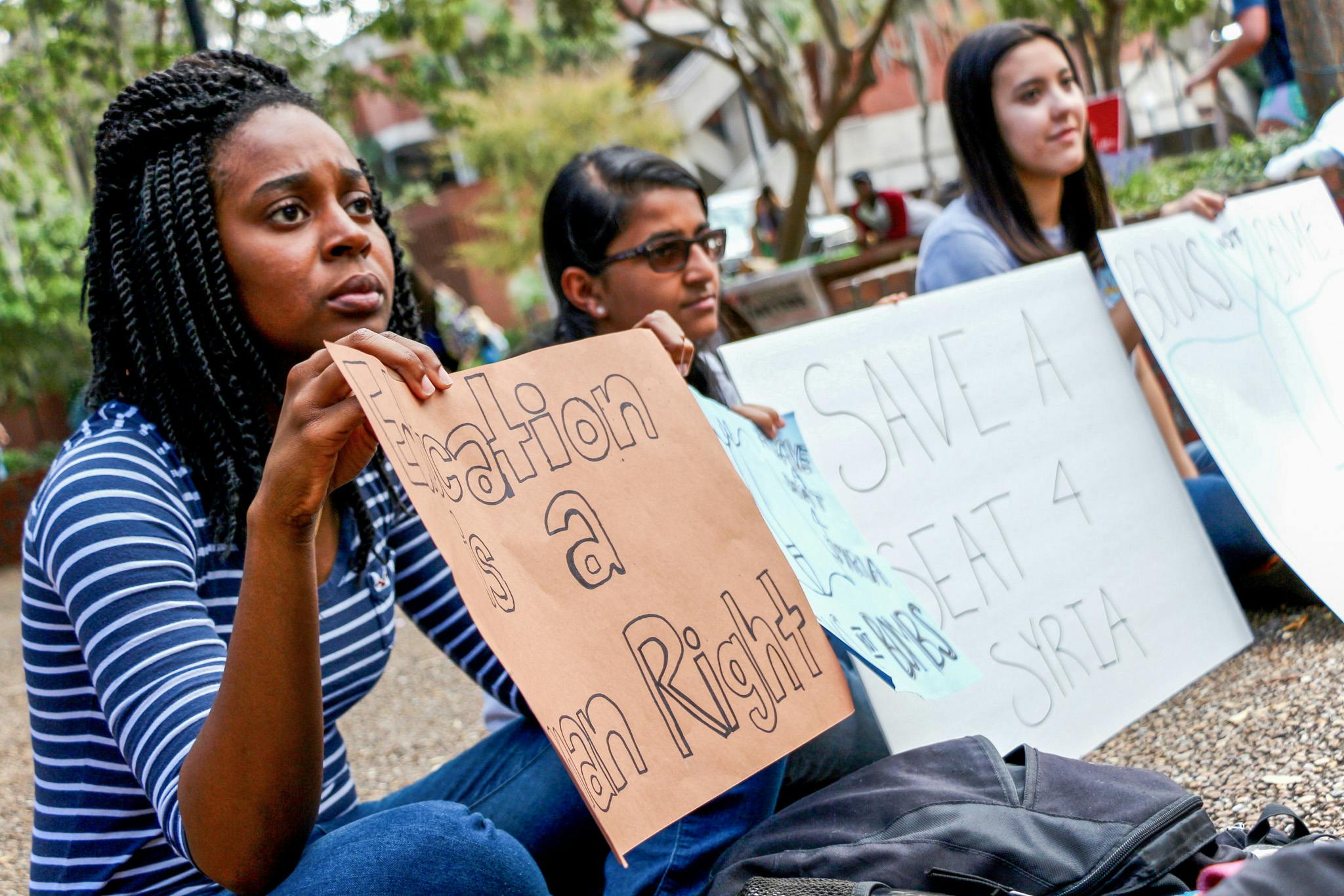 From left: Mashli Fleurestil, a 22-year-old UF biology senior; Rebecca Prince, an 18-year-old UF health science freshman; and Mariana Suguieda, a 19-year-old UF microbiology and cell science sophomore, hold signs to encourage students to sign a petition to bring Syrian refugees to UF. 