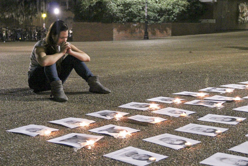 Michelle Zamperlini, an 18-year-old UF exploratory freshman, sits in front of the photos of the 43 protesters who went missing in Ayotzinapa, Mexico on Turlington Plaza Thursday evening. “One of them looks exactly like my cousin,” she says, as she clasps her hands in remembrance of the lives that were lost.