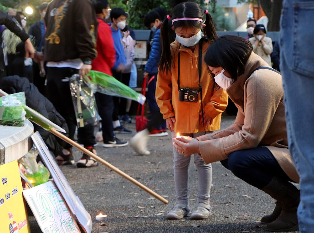 <p>Iris Wang, 6, (left) watches Minmin Jin, 43, a Gainesville resident (right), light a candle in front of Turlington Plaza Saturday, March 20, 2021. The two stood with a large crowd commemorating the tragedy in Atlanta and calling attention to racism against Asian Americans.</p>