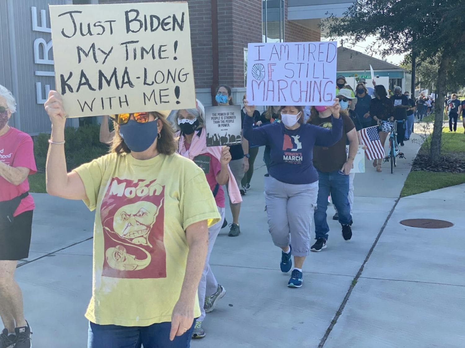 Marchers carry signs with messages such as “Just Biden my time! Kama-long with me!” and “I am tired of still marching” in support of Democratic presidential nominee Joe Biden and vice presidential nominee Kamala Harris.