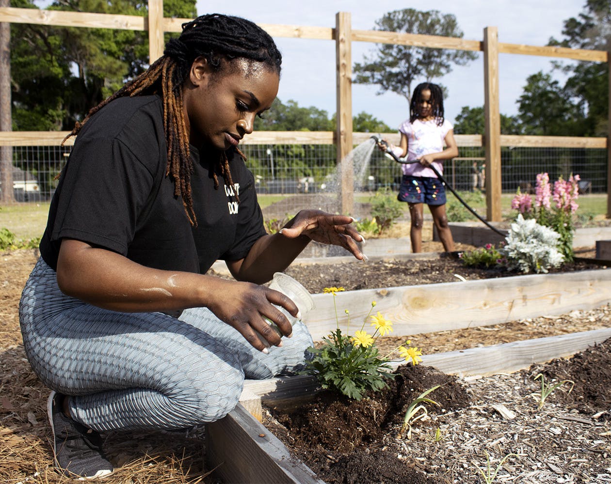 Kimberly Brown, 30 (left), sprinkles fertilizer around newly planted daises as her 7-year-old daughter, Bella Smith (right), waters a garden plot behind her on Monday, March 29, 2021. They spent the day at Reserve Park for the second Gainesville Black Garden Network meeting since the group formed in February.