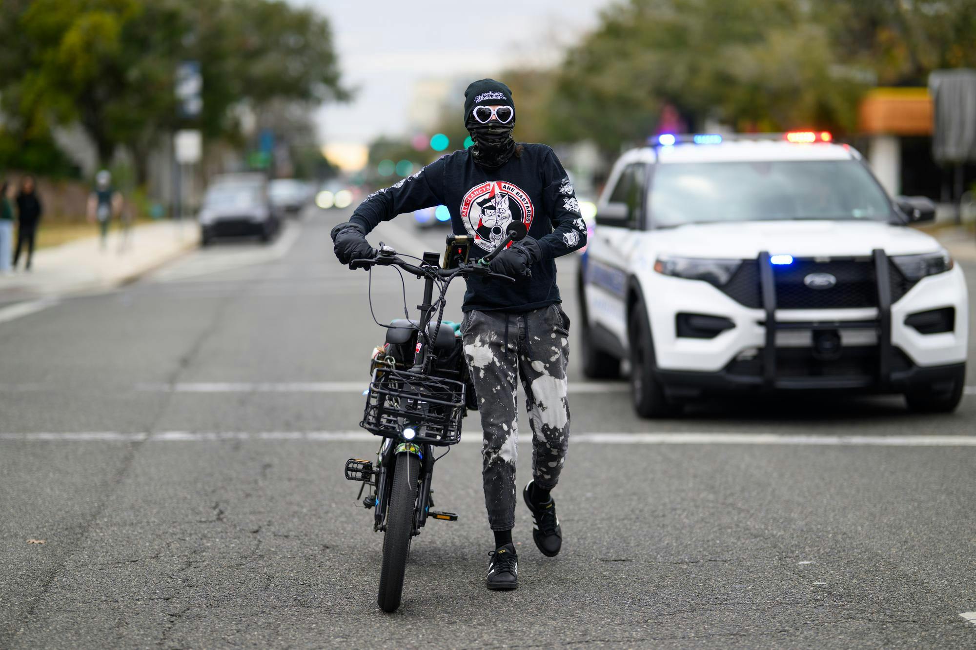 A masked man with a bike and speaker approaches demonstrators during an ICE protest organized by YDSA, Friday, Jan. 30, 2026, along University Avenue in Gainesville, Fla.