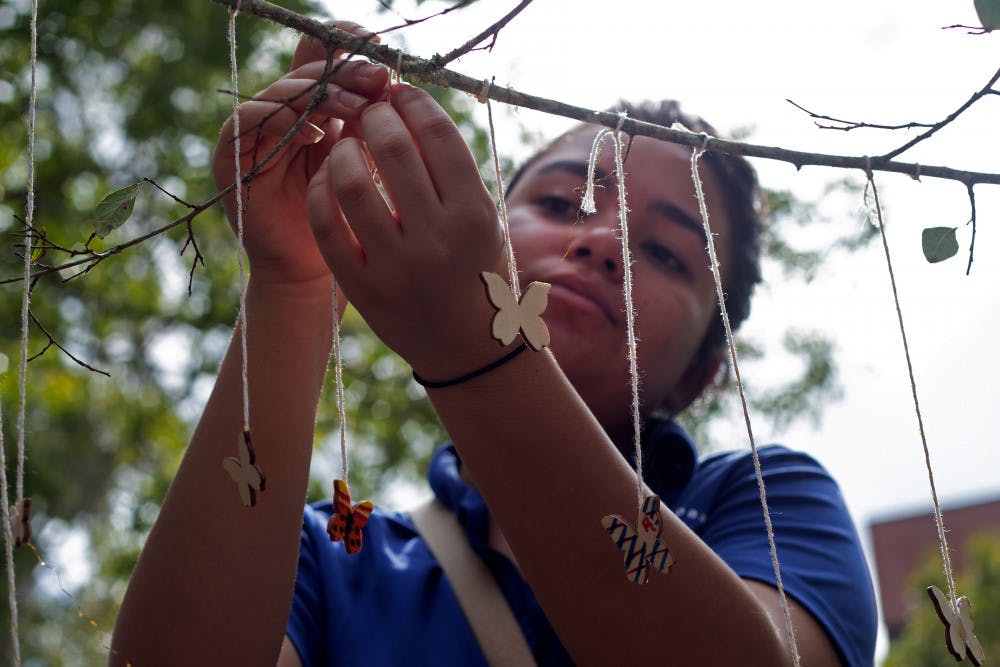 Bianca Cegatte, the vice president of marketing for Chispas UF, hangs a butterfly on a tree Tuesday afternoon in Turlington Plaza as part of the “I Stand With Immigrants Day of Action.” The event, hosted by Chispas UF, invited students to paint small wooden butterflies with the colors of their home country’s flag or colors that represented something important to them. 