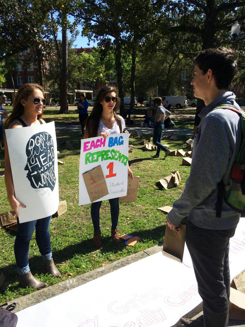 <p>Michelle Smith, a 20-year-old UF health science sophomore, and Christine Marino, a 21-year-old UF health education and behavior junior, talk to Joseph Buss, a 19-year-old UF economics sophomore, during Alpha Epsilon Delta’s “Every Gator Counts” event. The pre-health honor society passed out 400 paper bags holding anonymous stories of AED members’ struggles with mental illness to let students know they’re not alone.</p>