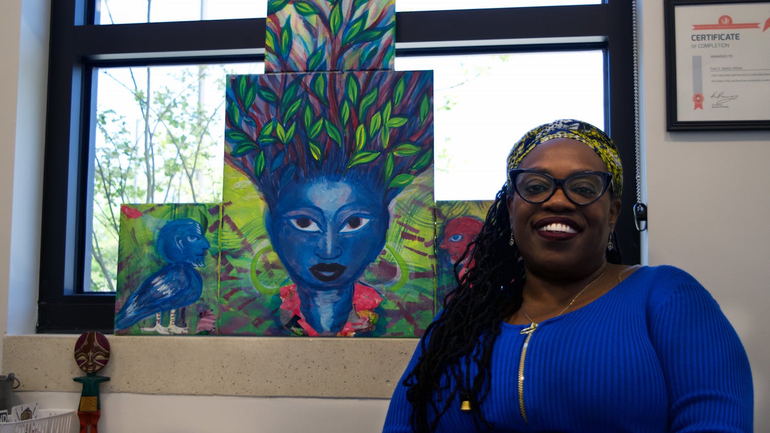 Terri Bailey sits in front of “Iya,” a painting created by Turbado Marabou, in Blount Hall Sunday, March 18, 2023.