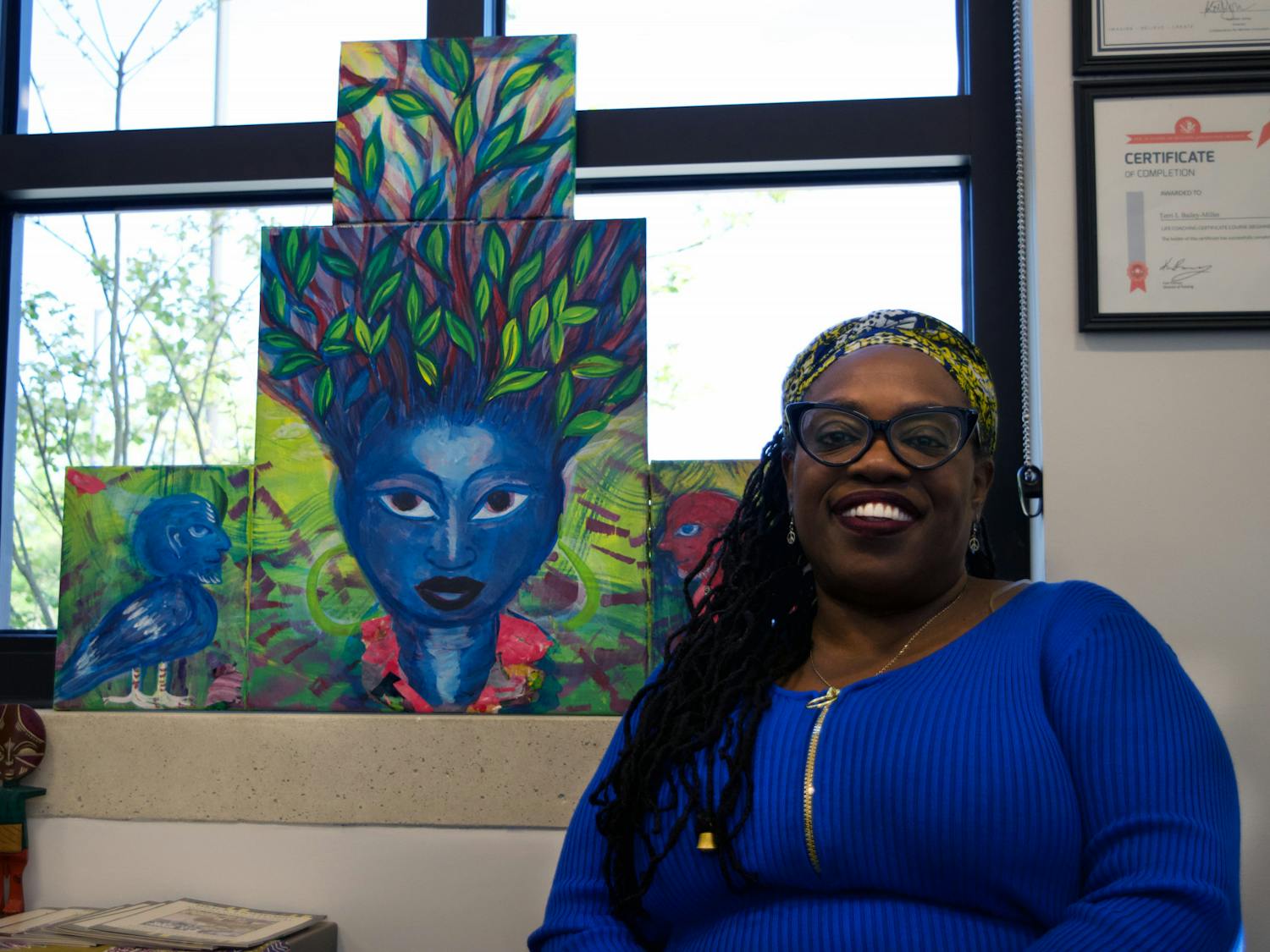 Terri Bailey sits in front of “Iya,” a painting created by Turbado Marabou, in Blount Hall Sunday, March 18, 2023.