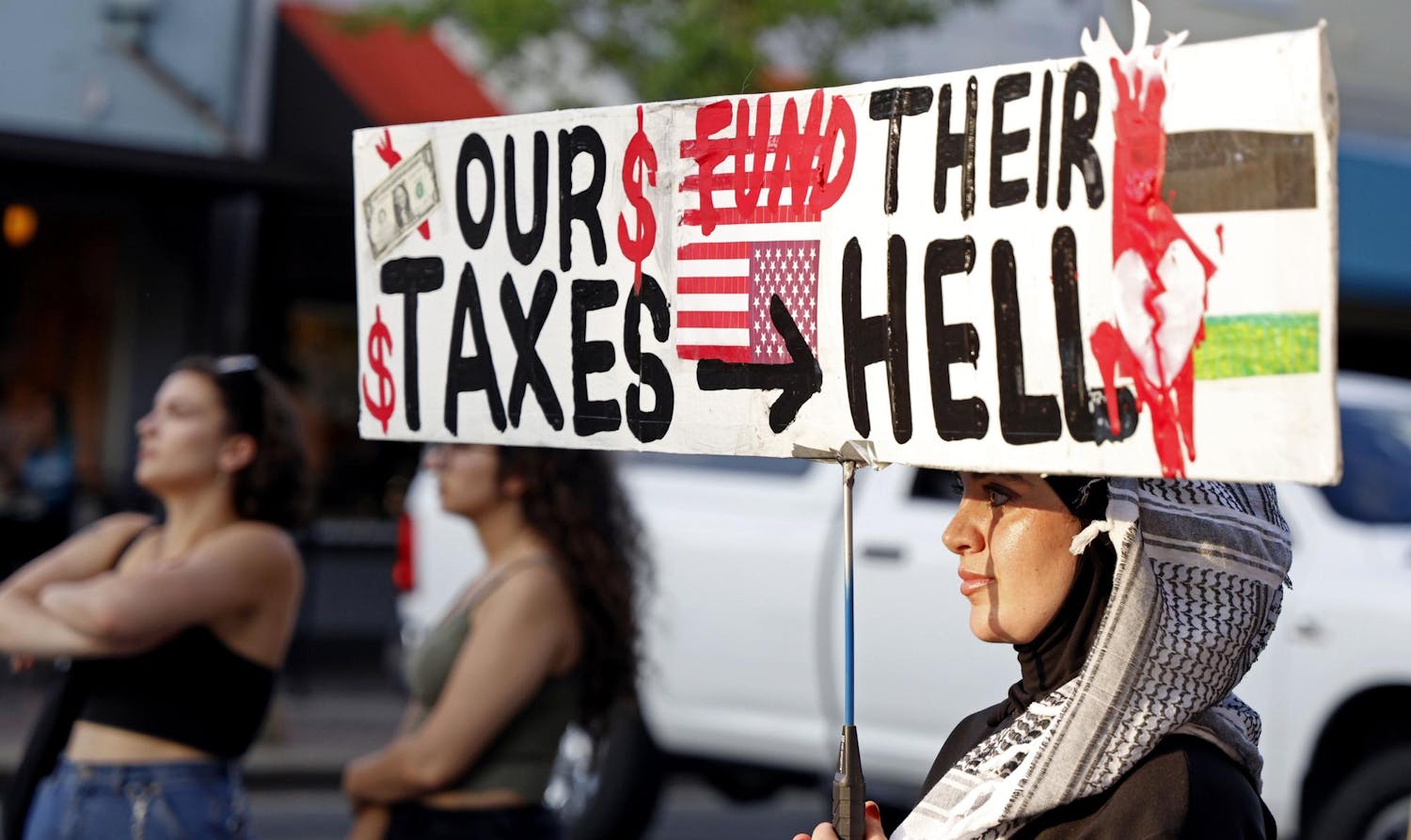 A protestor holds a sign reading "Our Taxes Fund Their Hell" during a protest in downtown Gainesville on Monday, May 27, 2024.