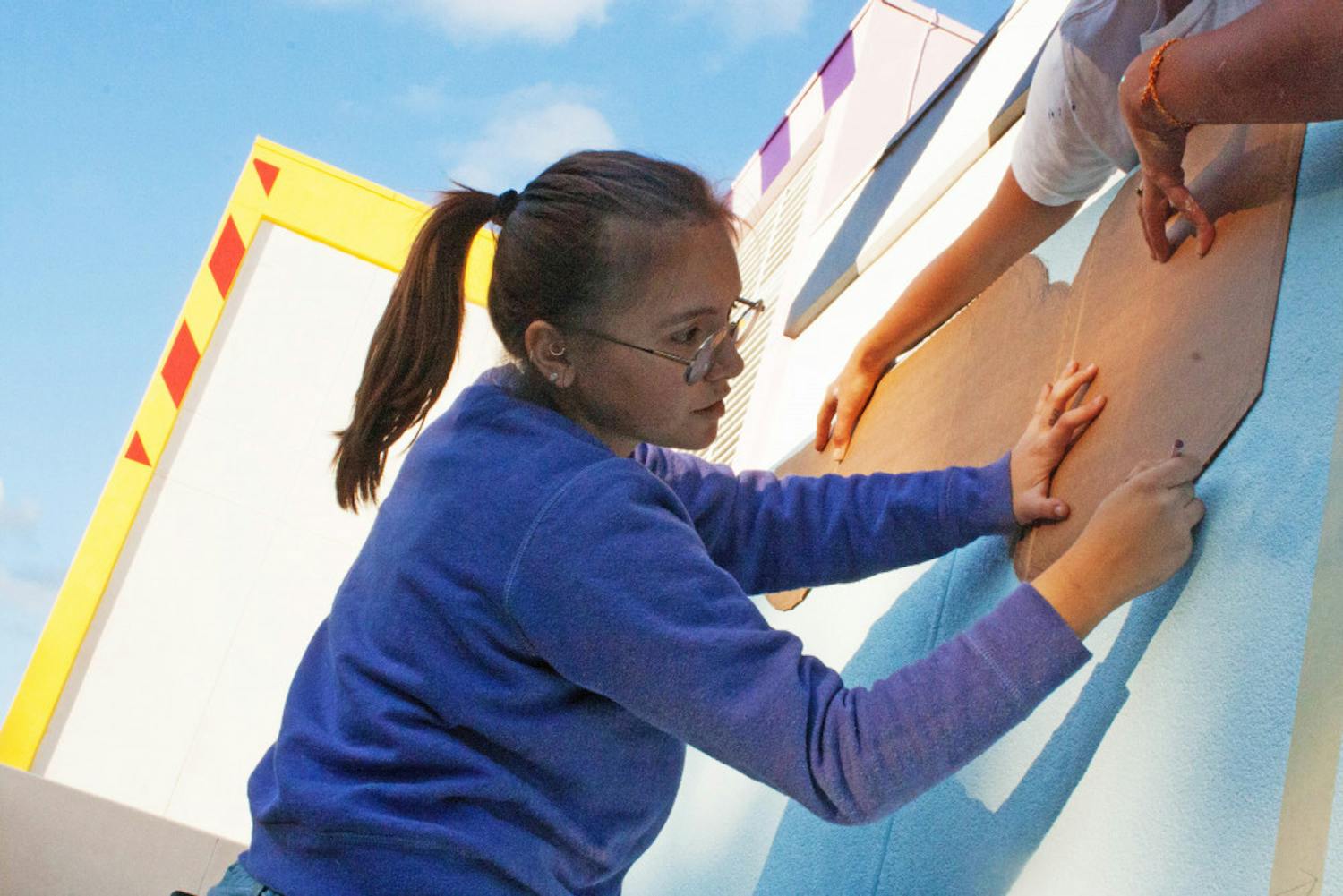 Jovana Christiani, a 19-year-old Santa Fe College illustration sophomore, outlines the new mural on Santa Fe’s walls Tuesday. The mural is set to be finished Saturday.