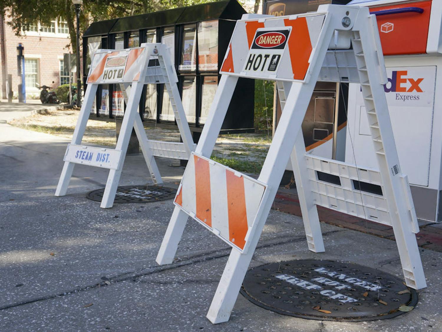 Safety barriers cover manholes emitting hot steam on the sidewalk along Stadium Road. 