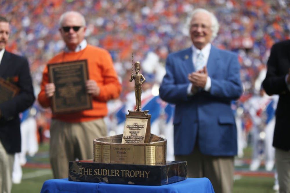 <p>UF President Bernie Machen,&nbsp;<span>associate director of bands</span> <span>Jay Watkins and others pose behind the Sudler Trophy during Saturday’s Homecoming game halftime show.</span></p>
