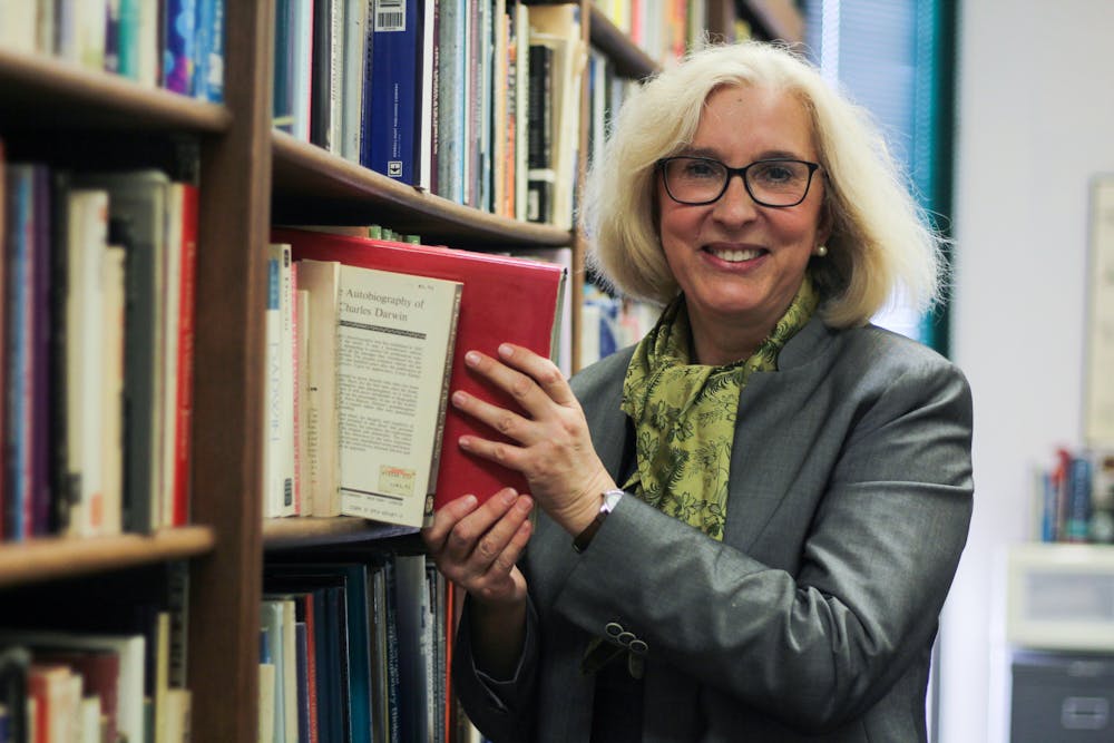 <p>Wearing a green silk scarf gifted to her by a student, Vassiliki Betty Smocovitis pulls a book from the shelf in her office, located in Carr Hall, Friday, March 31, 2023. </p>