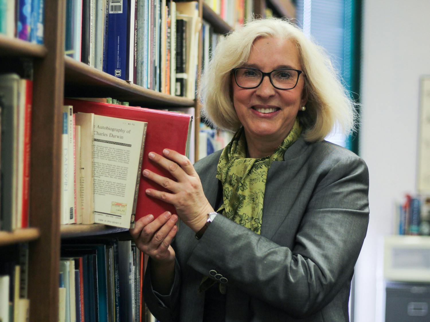 Wearing a green silk scarf gifted to her by a student, Vassiliki Betty Smocovitis pulls a book from the shelf in her office, located in Carr Hall, Friday, March 31, 2023.