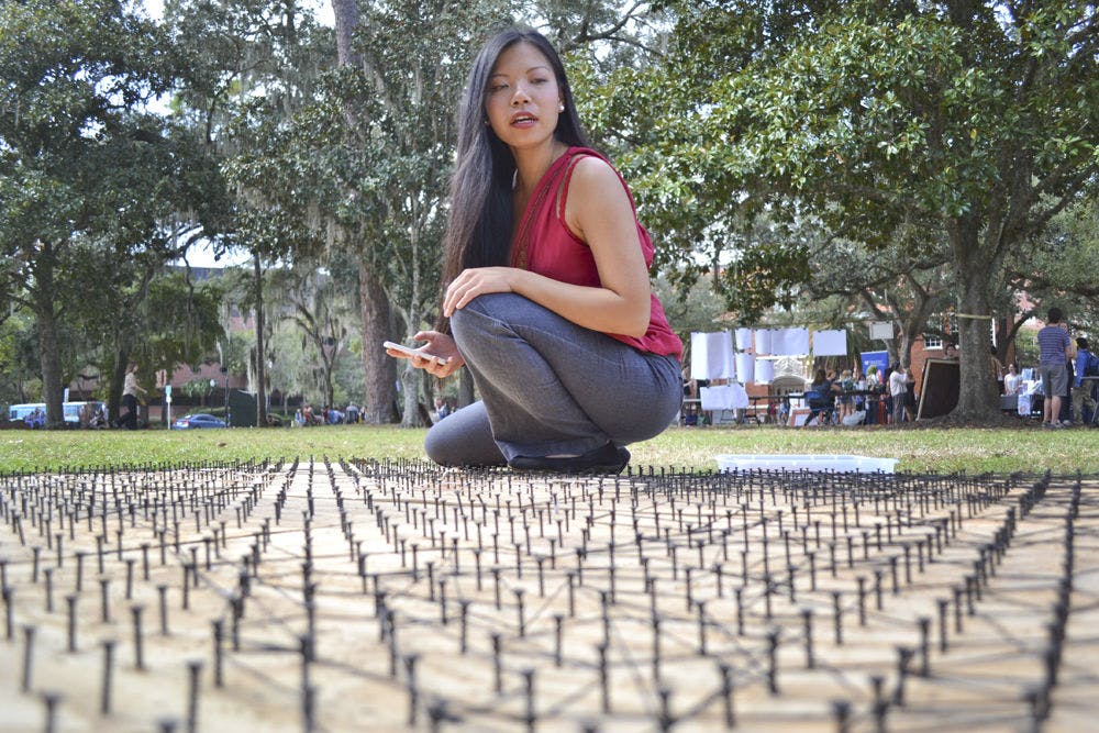 <p>Sitting on a wooden bed of screws and rubber bands, UF anthropology junior Van Truong, 20, scans over an incomplete 6 foot by 8 foot Mona Lisa art piece at the Pop-Up Culture event on the Plaza of the Americas on Oct. 14, 2015. Truong, who helped put the event together, opened her project to all students at the event to gather “inspiration from other people who approach art and life differently.”</p>
