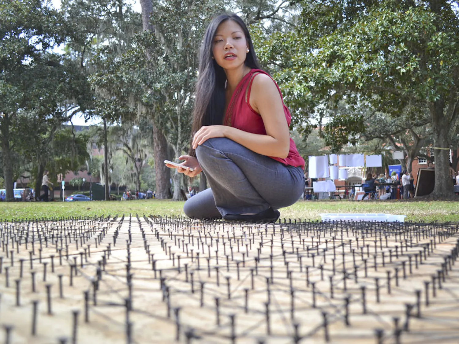 Sitting on a wooden bed of screws and rubber bands, UF anthropology junior Van Truong, 20, scans over an incomplete 6 foot by 8 foot Mona Lisa art piece at the Pop-Up Culture event on the Plaza of the Americas on Oct. 14, 2015. Truong, who helped put the event together, opened her project to all students at the event to gather “inspiration from other people who approach art and life differently.”