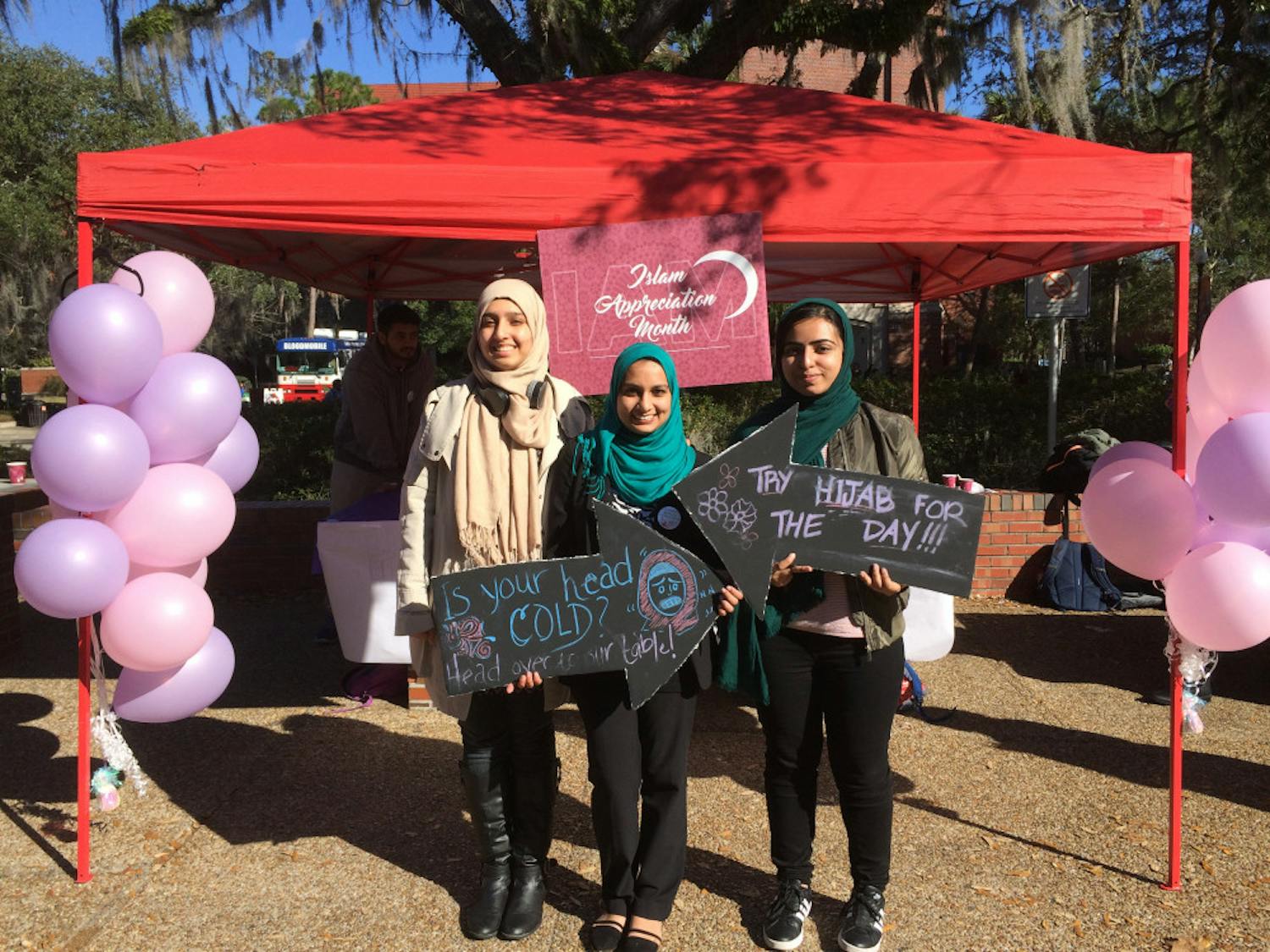 Huda Aziz, Adeeba Ahmad and Maliha Khan post with "Hijab-a-Thon" signs after helping UF students Wednesday try on the headscarf.