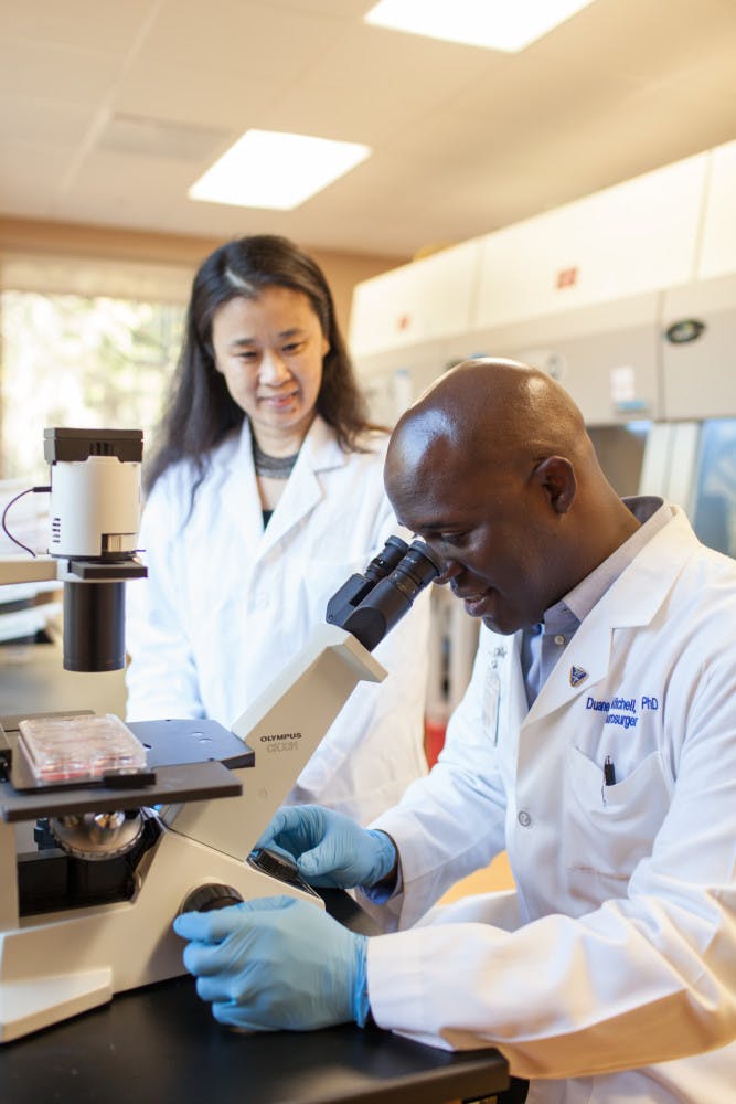 Duane Mitchell and Dr. Jianping Huang, Director of Clinical Laboratory Operations for the UF Brain Tumor Immunotherapy Program, work together on research in a laboratory. 