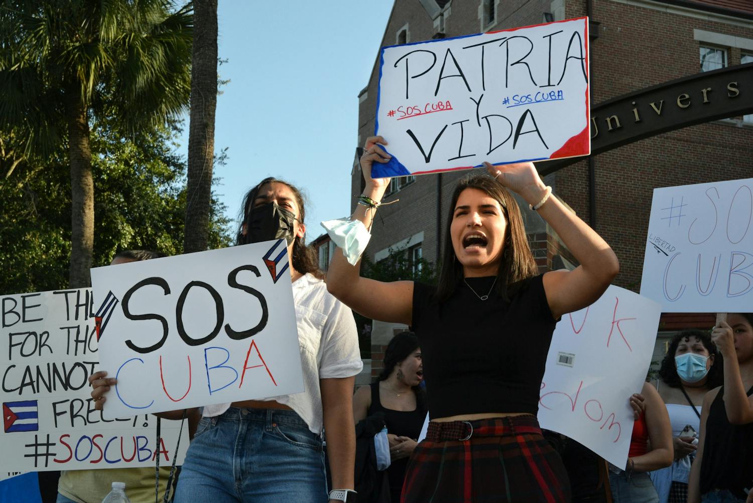 Marian Hernandez, 21, a psychology senior, (right), and Jenna Hidalgo, 21, a criminology and psychology senior, (left), shout “Patria y Vida” as they raise signs embellished with colors of the Cuban flag on Friday, July 16, 2021. UF students gathered at the corner of University Avenue and 13th street to protest human rights abuses in Cuba.