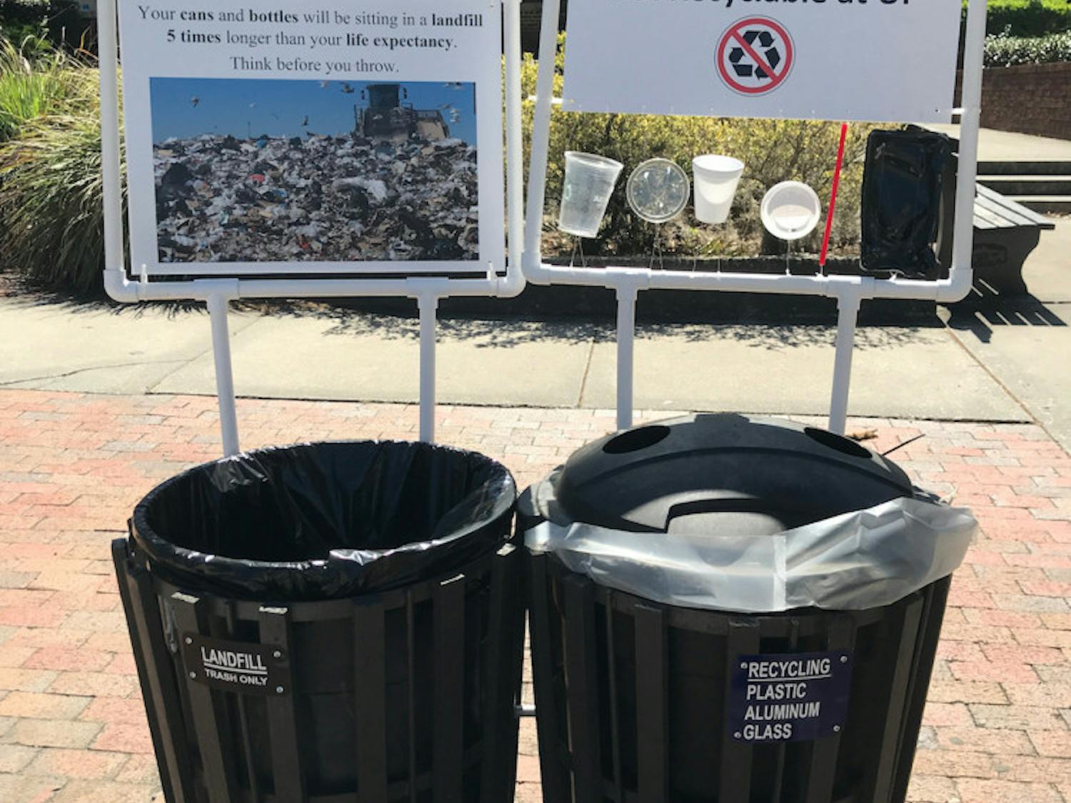 Pictured is a pair signs framed by PVC pipes hanging next to a set of trash and recycling cans that appeared on campus early Monday morning. The signs are part of a student research project by UF/IFAS first-year PhD student Amanda Brinton. The signs will be up until April 20, she said.