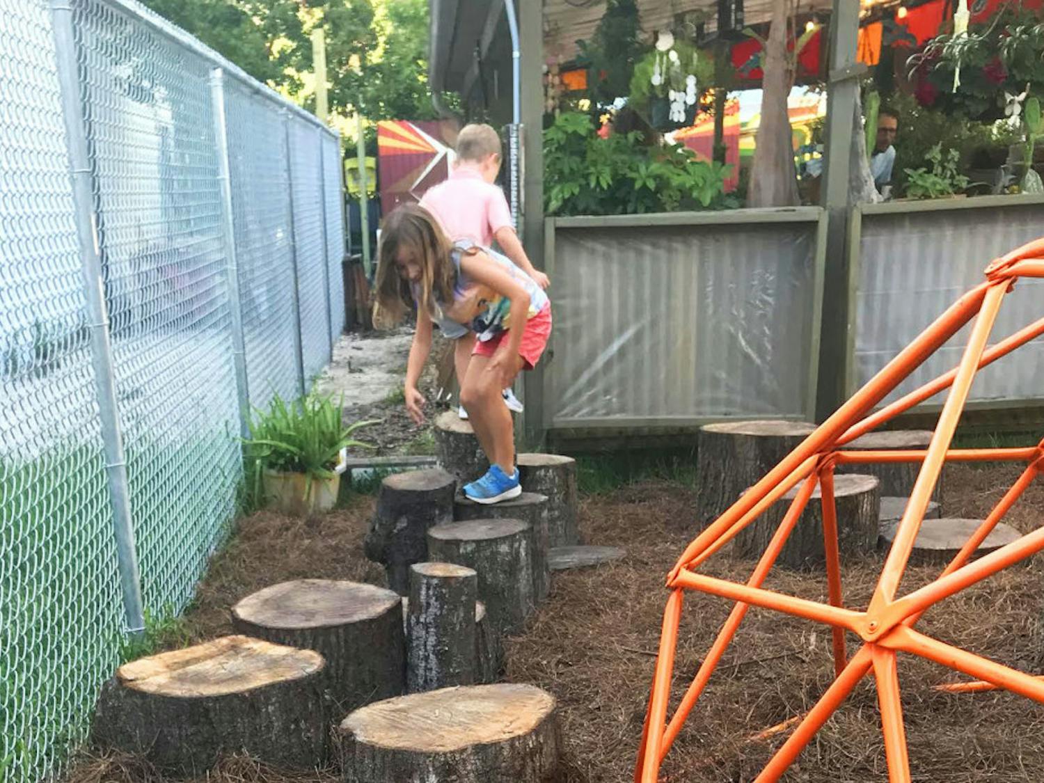 Children play on new tree stumps next to a repurposed orange dome that survived a fire at Satchel's Pizza almost two years ago.